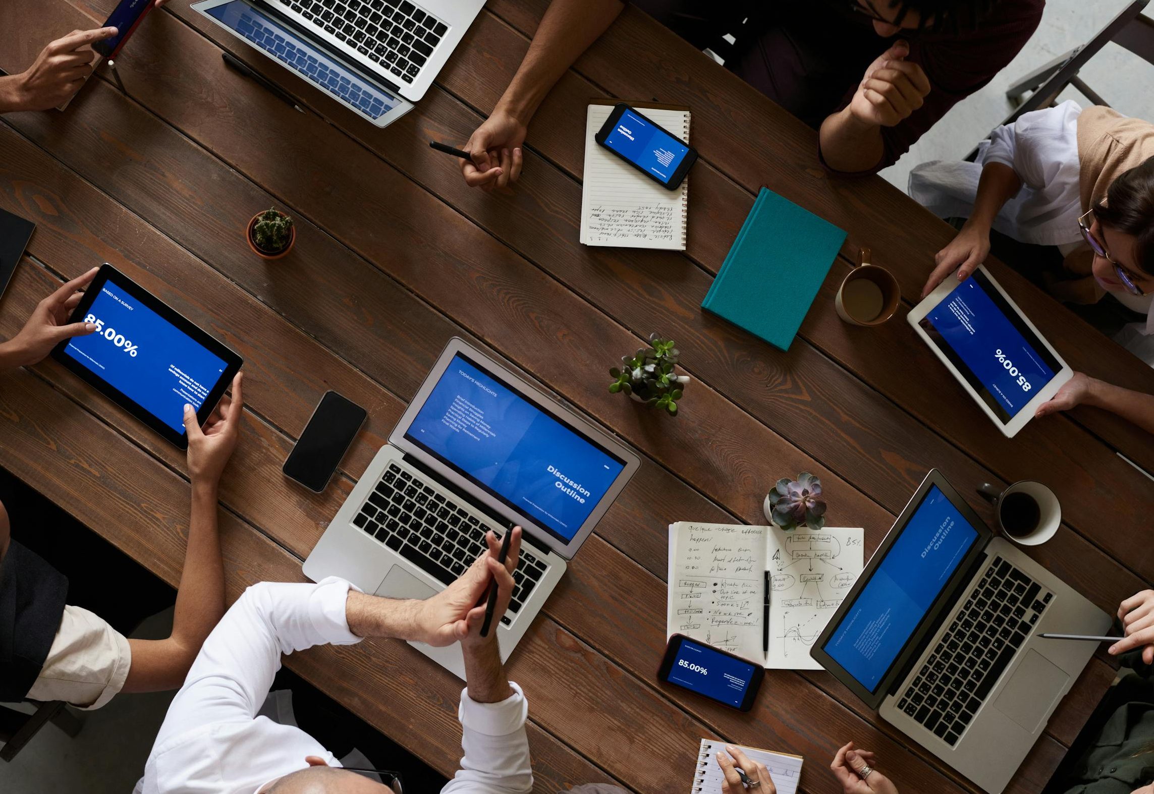 Overhead view of a diverse team at Streamline Your Work discussing around a wooden table, using technology.